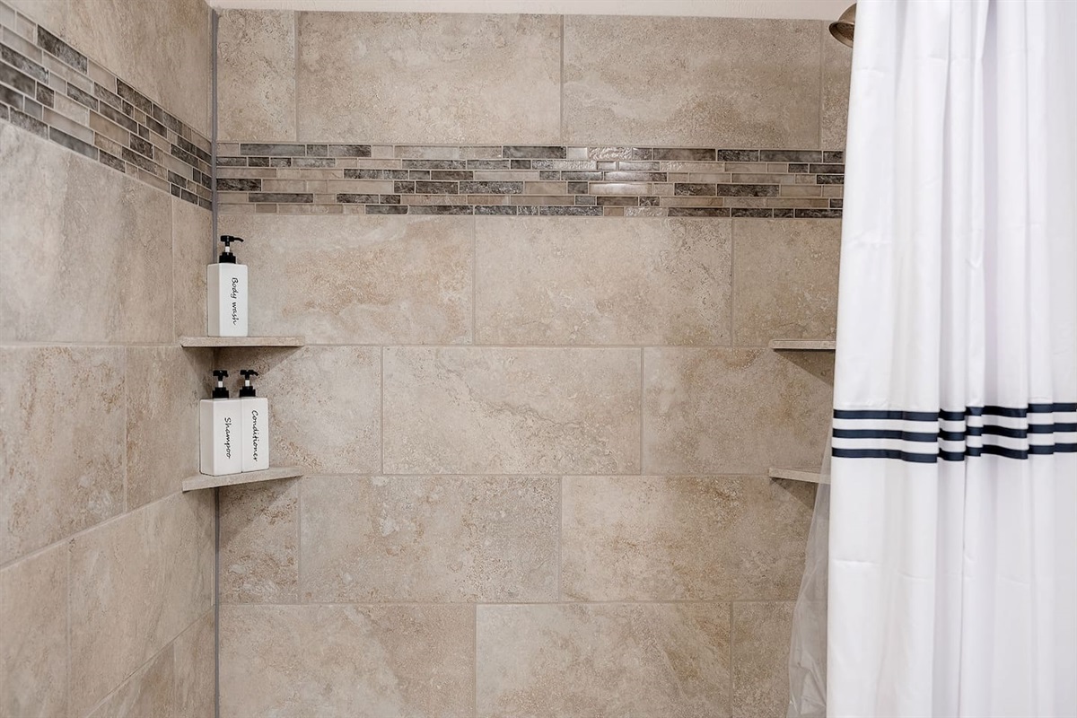 Enjoy a spacious shower area featuring elegant tile work and built-in shelves. The provided toiletries add to the convenience and comfort.