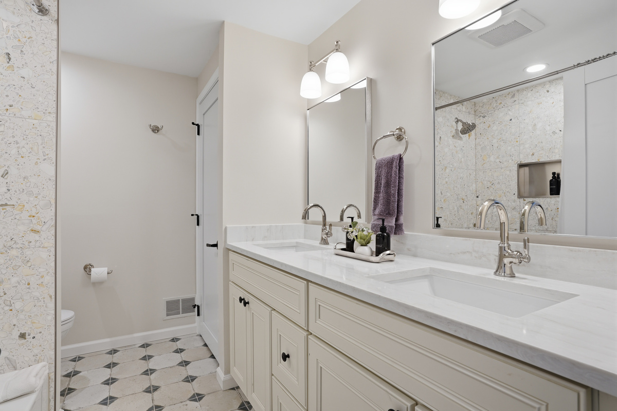 Bright, modern spa-style bathroom with dual quartz vanities, polished finishes, and a walk-in shower. Clean, spacious design with soft lighting creates a fresh, hotel-like feel.