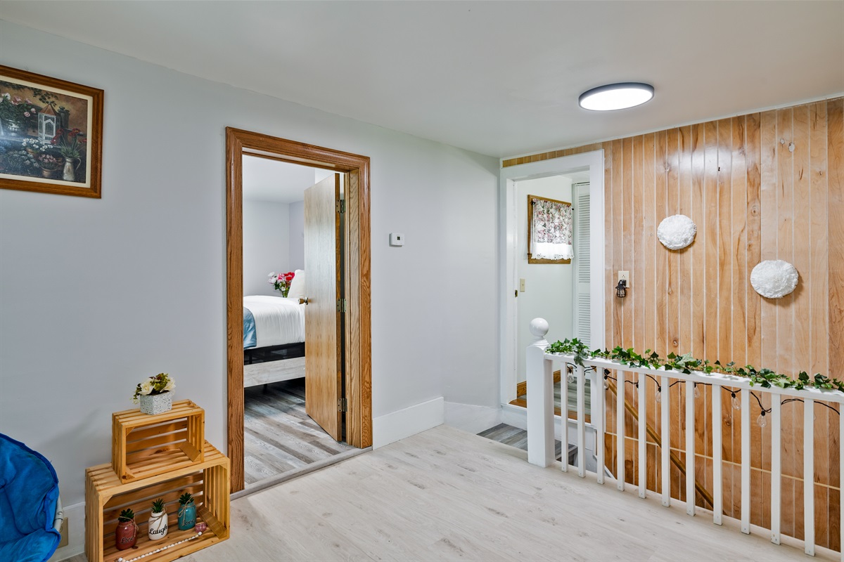 Charming upstairs hallway with rustic accents, bright lighting, and cozy decor leading into two inviting bedrooms.