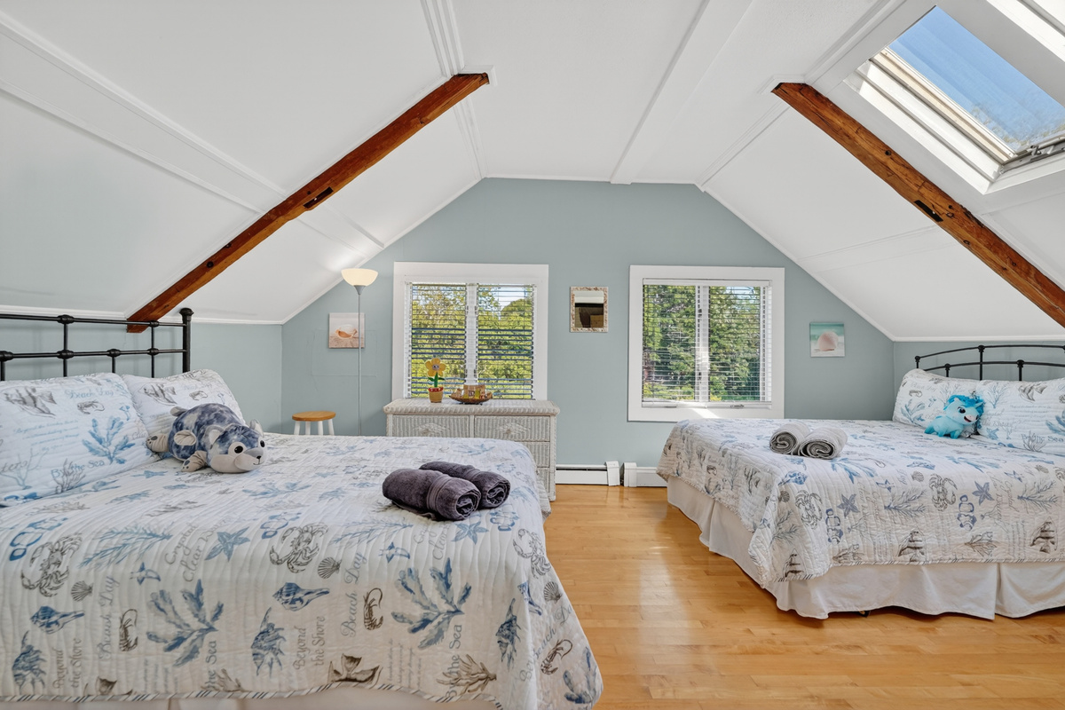 Spacious upstairs bedroom with two comfortable beds, vaulted ceilings, and plenty of natural light.