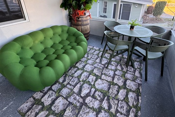 Spacious outdoor patio at Mario's Mini Mansion in Clermont, FL! Oversized green "football" couch, stone paver rugs, and dining table perfect for relaxing or enjoying meals al fresco with the whole family. Bamboo shades can unroll for extra privacy!