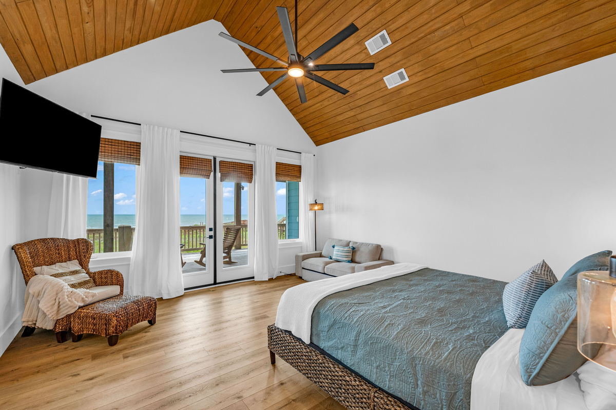 Cair Paravel: The primary suite stretches out beneath a vaulted wood ceiling, with a mounted TV, private deck access, and a cozy reading chair for quiet mornings.
