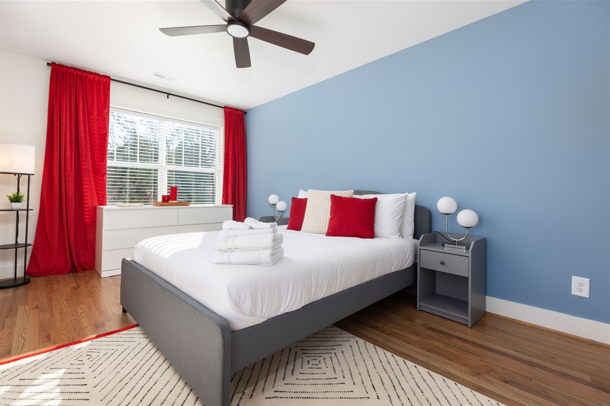 The upstairs queen bedroom has luxurious linens, blackout curtains, and an overhead ceiling fan for air flow for the best night's sleep.