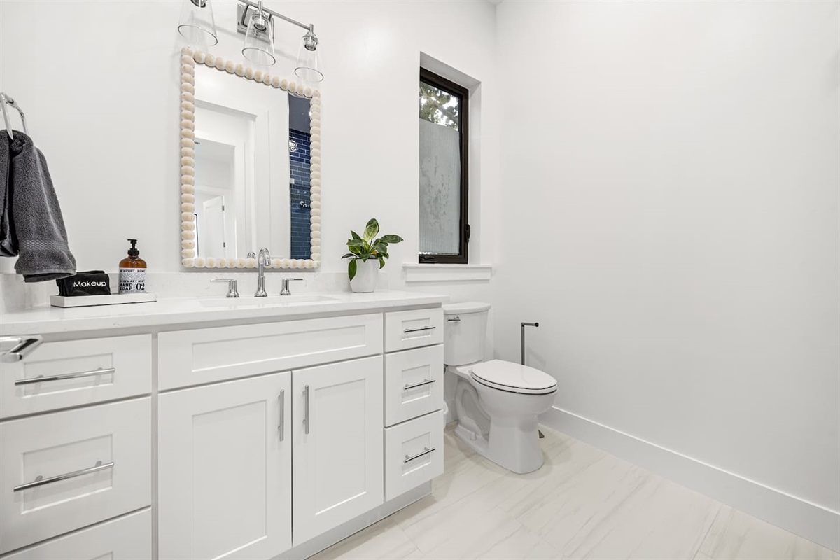 Step into this modern bathroom featuring a toilet with a window above, a sleek sink and faucet with a storage drawer, a wide mirror, a neatly placed towel, and bright lighting for a refreshing ambiance