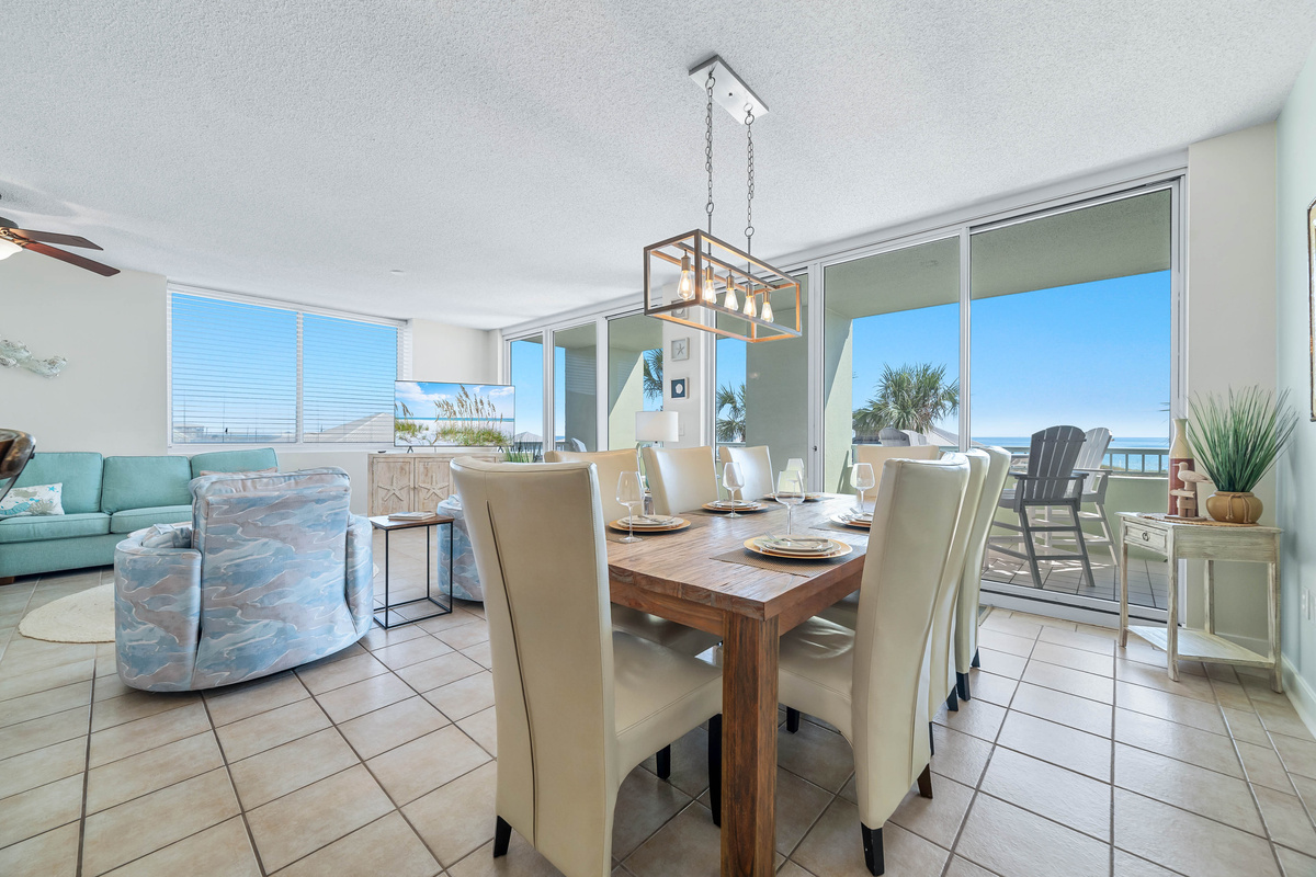 This inviting space features a large dining table, comfortable living area, and expansive sliding doors leading to a private balcony with ocean views.