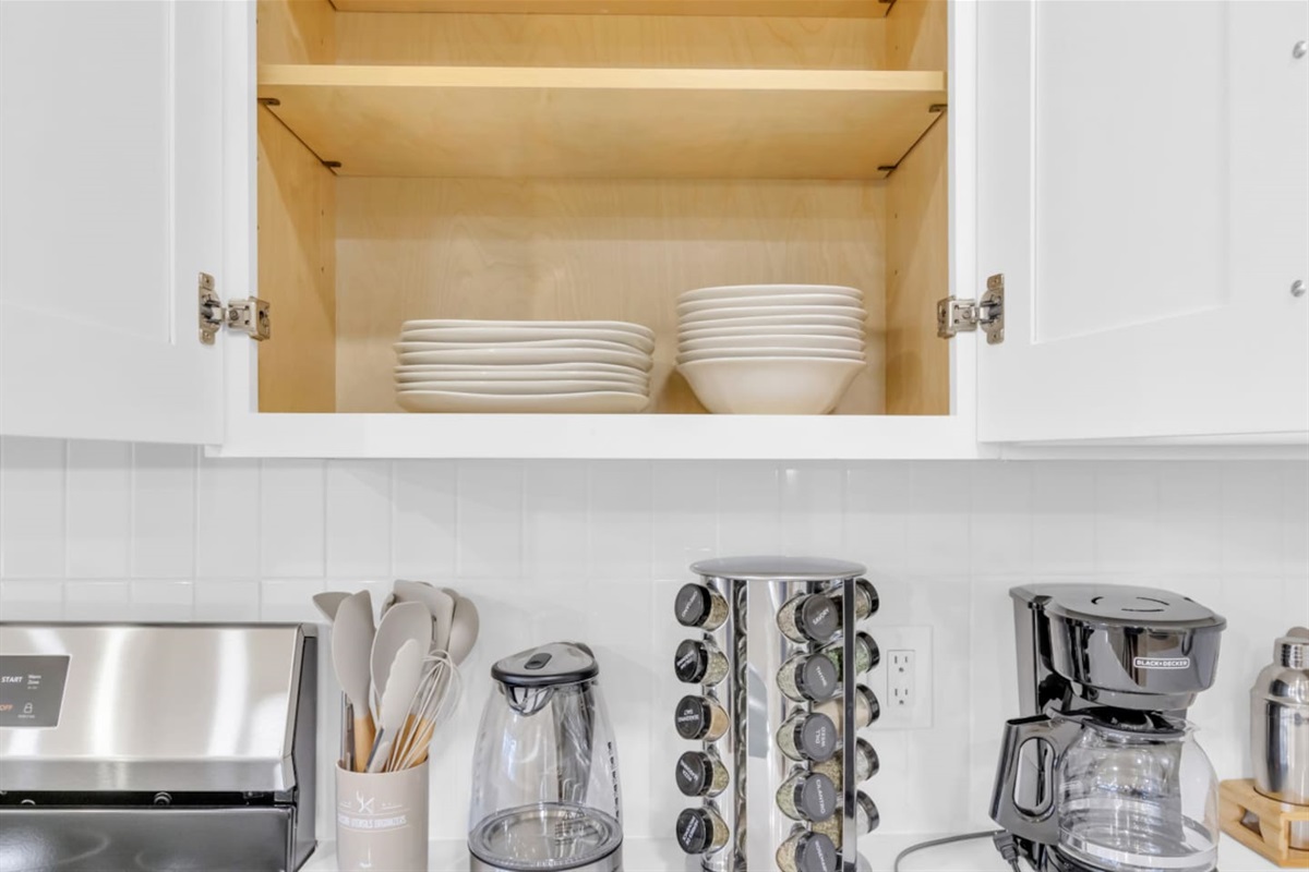 Open cabinet stocked with dishes and cutlery, bowls, and plates for group meals. Perfect for guests planning to enjoy the fully equipped kitchen.