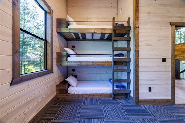 A modern cabin bunk room with stacked beds, cozy lighting, and a scenic window view of nature. This family-friendly lodging option is great for guests seeking comfort and style in a rustic retreat.