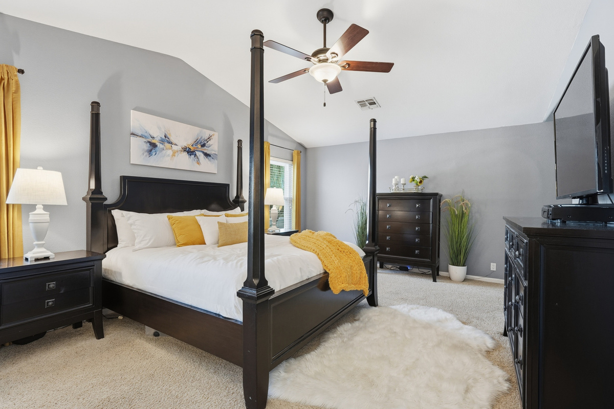 Primary bedroom with king bed, four-poster frame, sitting area, ceiling fan, and plenty of natural light.