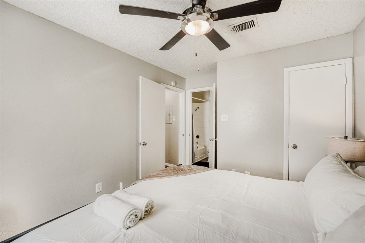 Bright, minimalist bedroom with neutral tones, a ceiling fan, and cozy bedding.