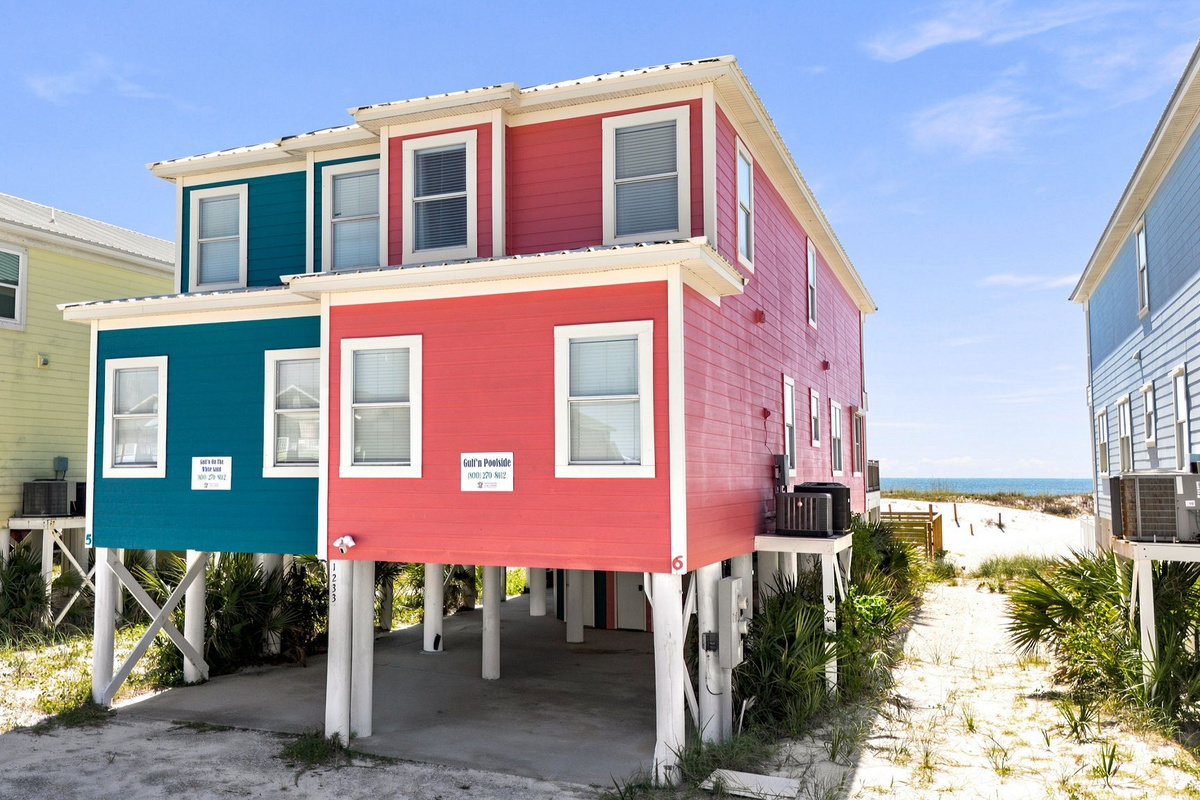 Exterior view of the colorful coastal vacation rental with elevated design, sandy surroundings, and convenient beach access nearby.
