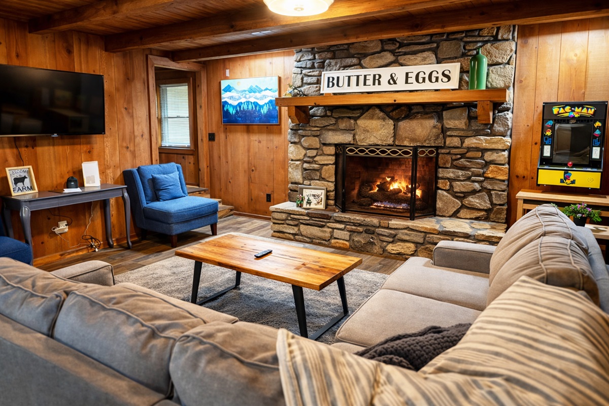 Gather around the stone fireplace after a day in the mountains—this cozy living room features plush seating, a Pac-Man arcade game, and the perfect cabin ambiance for relaxing nights in.