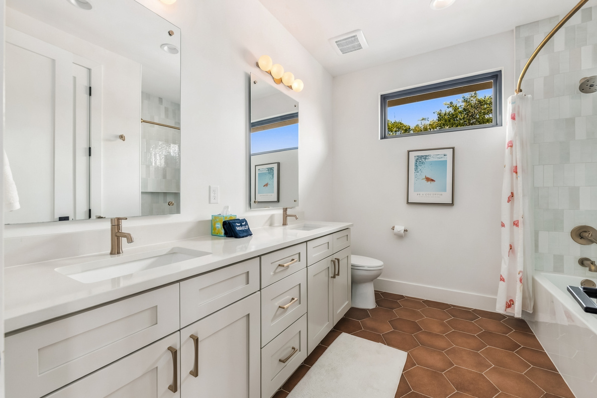 Bright vanity area with dual sinks and a window over the tub.