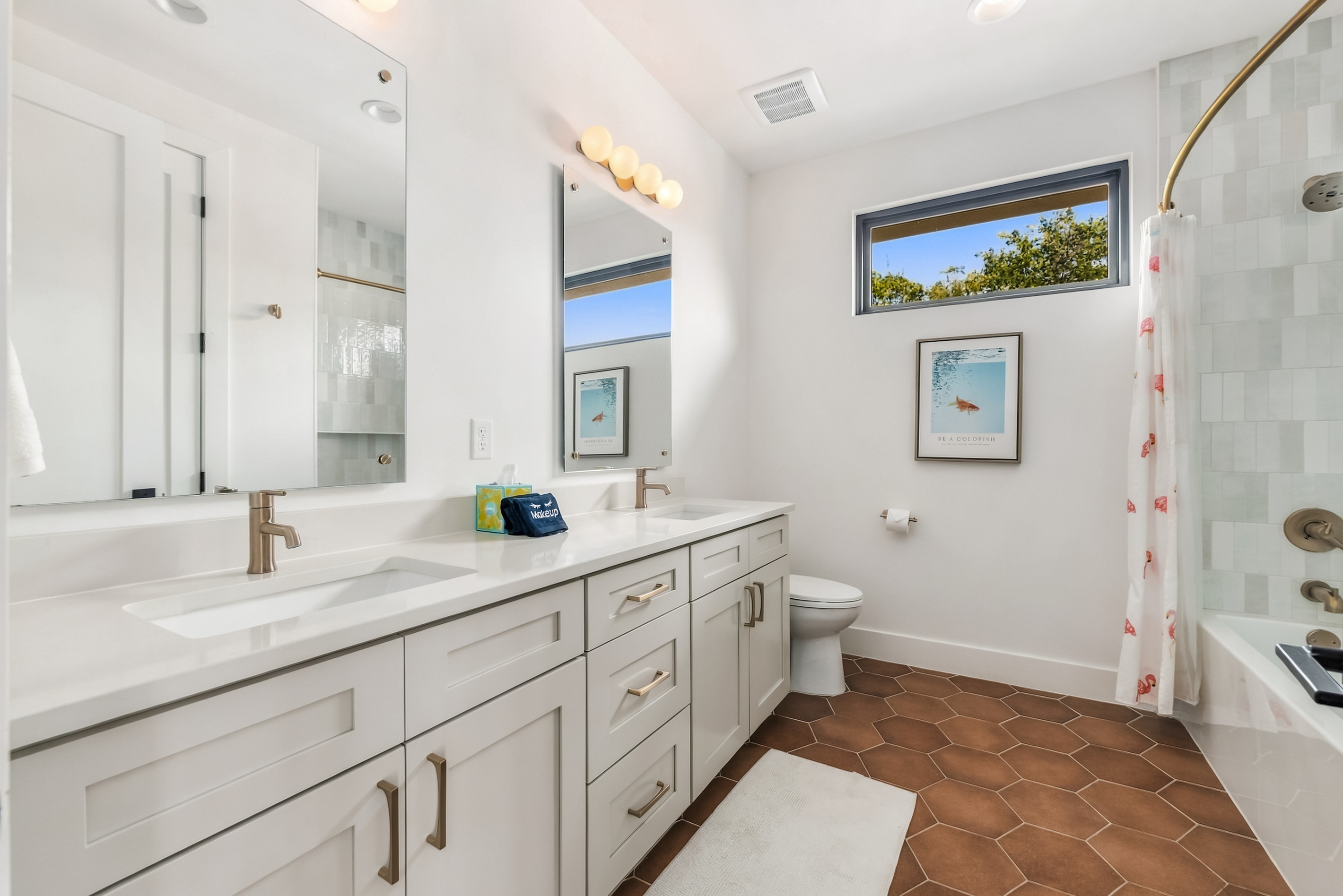 Bright vanity area with dual sinks and a window over the tub.