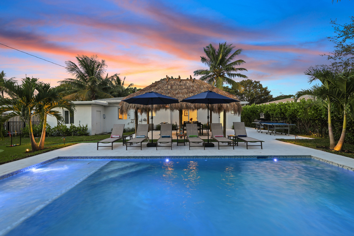 Start your Delray Beach getaway with this glowing twilight pool scene: Tiki hut, loungers, and resort-style outdoor space all made for relaxation.