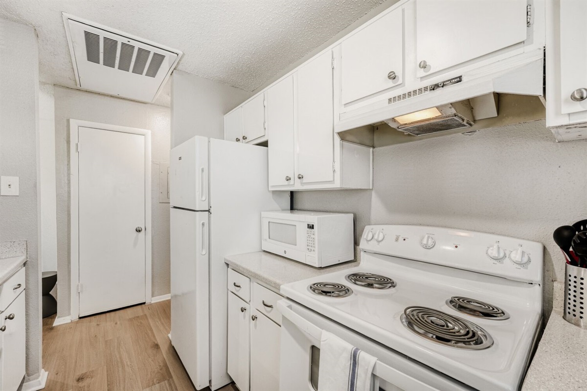 Bright, compact kitchen with white cabinetry, modern appliances, and wood-style flooring.