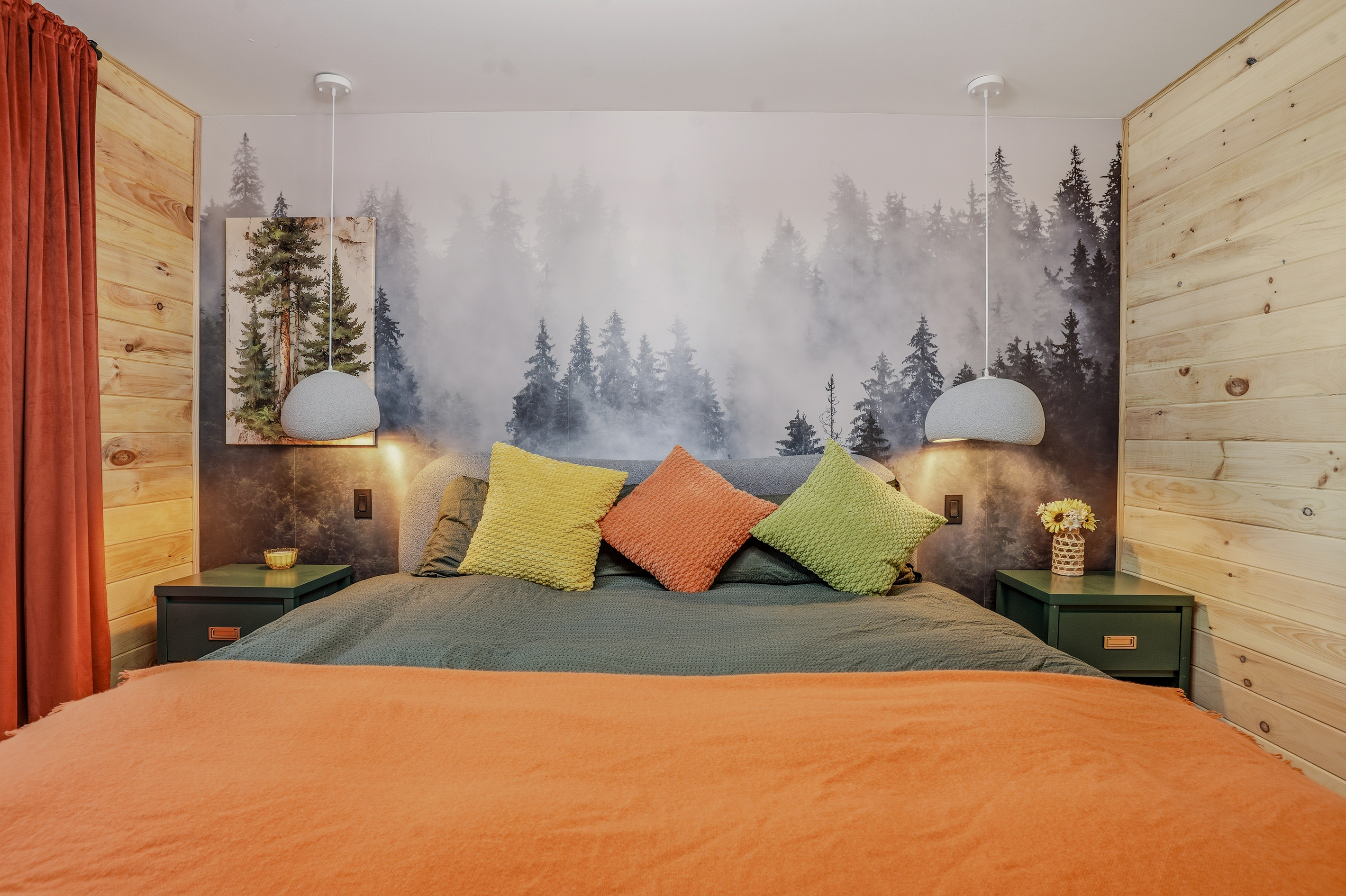 Primary bedroom with dramatic forest mural, king bed, warm pendant lighting, and teal curtains