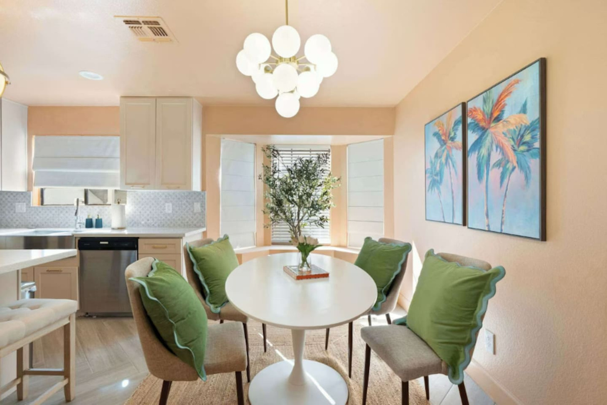 Bright dining nook with round white table, green upholstered chairs, and tropical art—a cheerful space for meals and conversation.