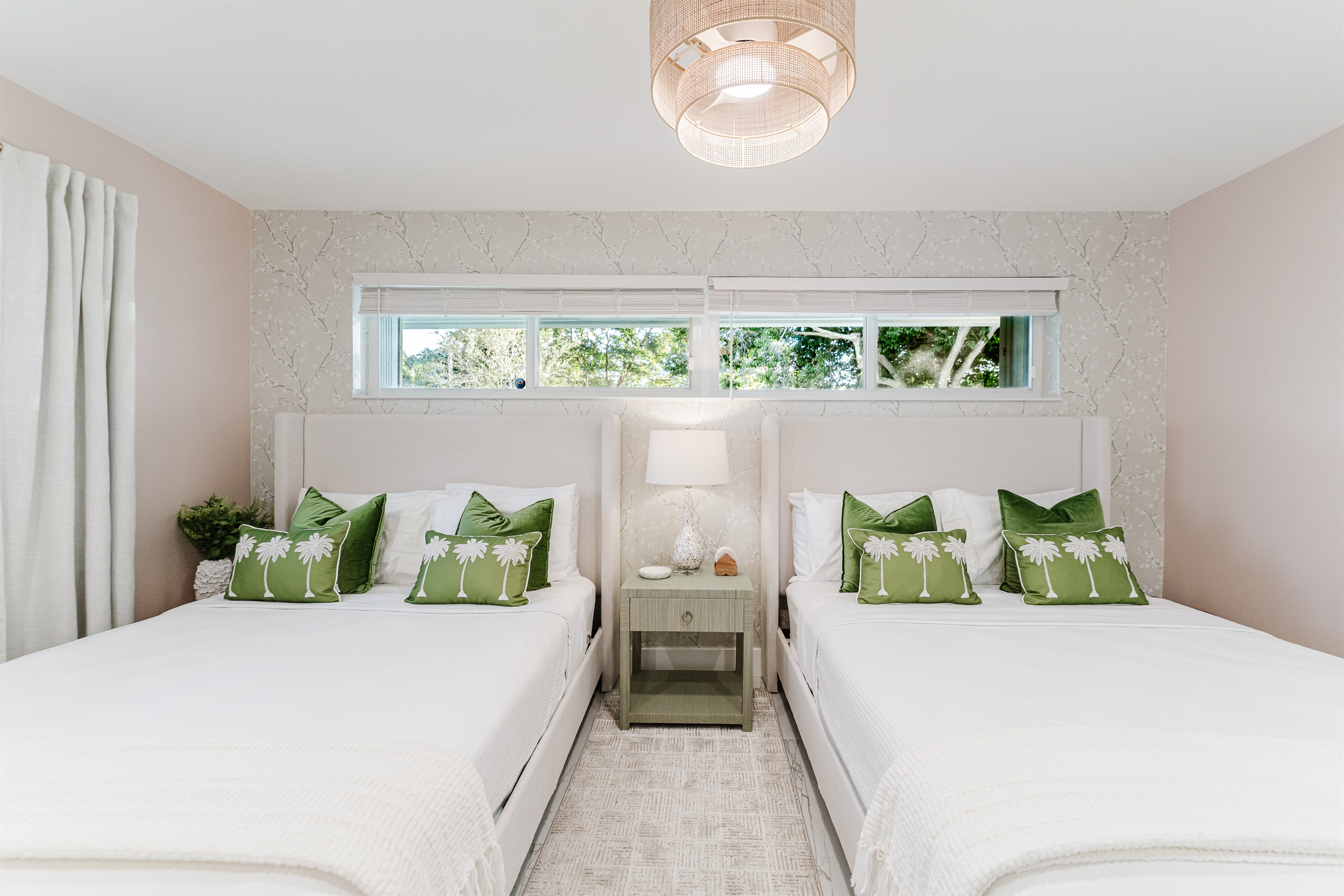 Bright, serene guest suite with two queen beds, hotel-quality linens, a wall-mounted smart TV, and ample storage. Features blackout curtains and blinds, a rattan ceiling fan, and a private en-suite bathroom—ideal for families or guests sharing space.