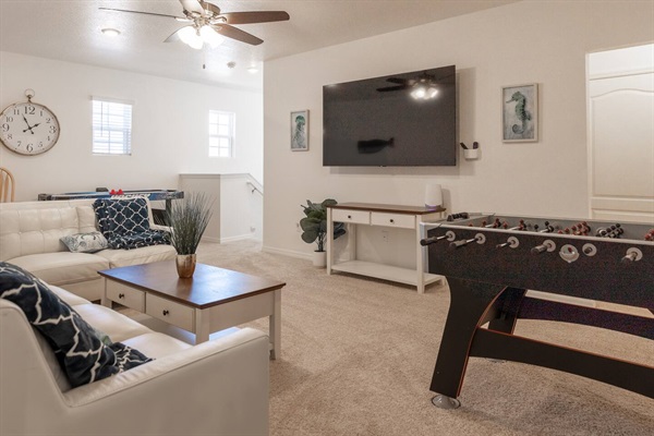 Upstairs lounge area with couch, 75in smart TV, overhead fan, air hockey table, foosball table and two player arcade game with thousands of games. 