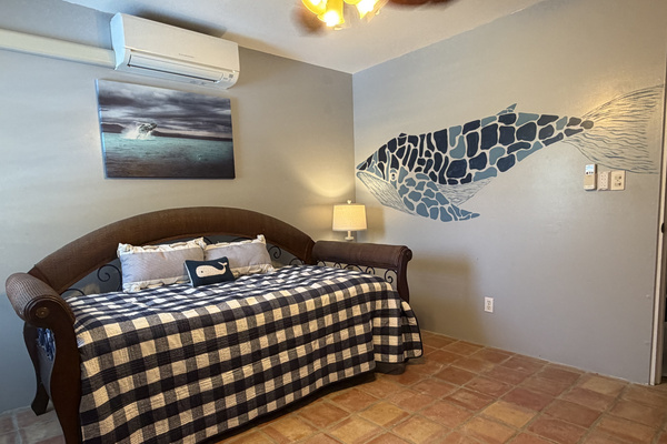 Features a versatile daybed with a pull-out trundle. Highlighted by a hand-painted mosaic whale mural and marine art, this room offers split-system AC, classic Saltillo tile floors, a tall distressed dresser, and a cozy bedside lamp with USB ports