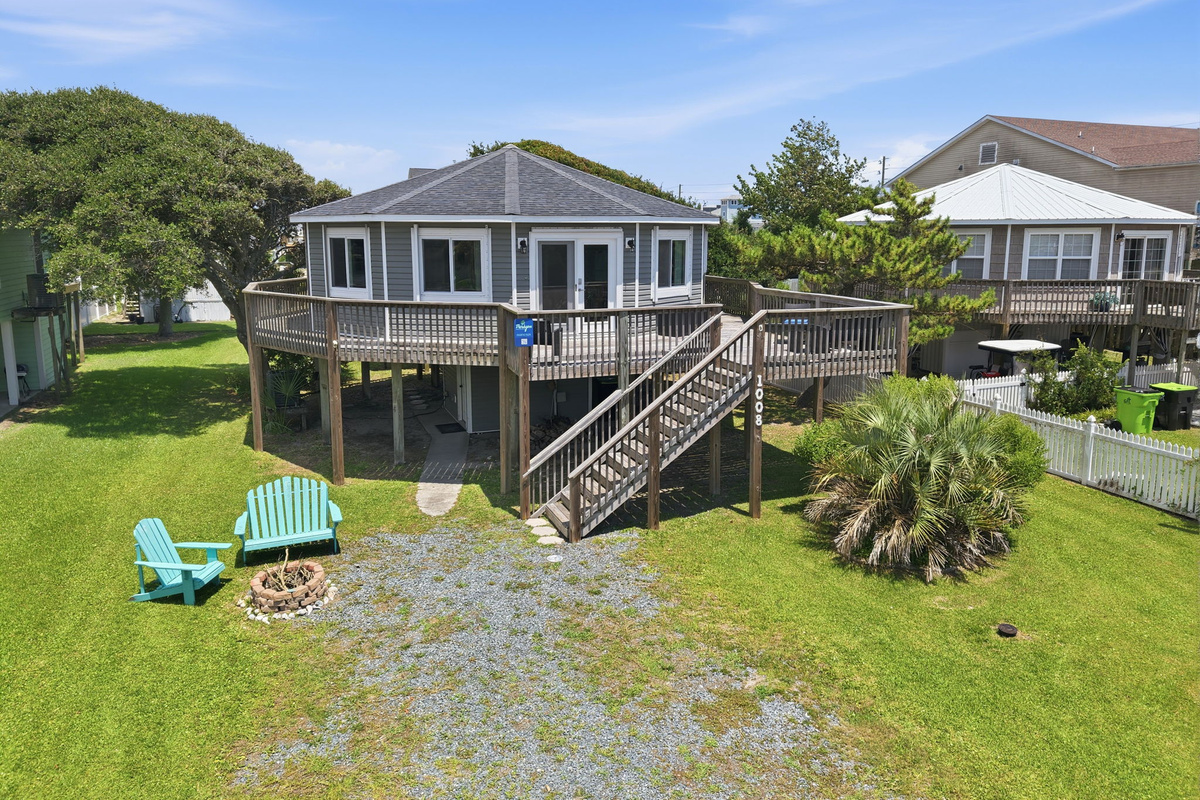 Exterior view of the home featuring wraparound decking, a spacious yard, and a cozy fire pit with Adirondack chairs