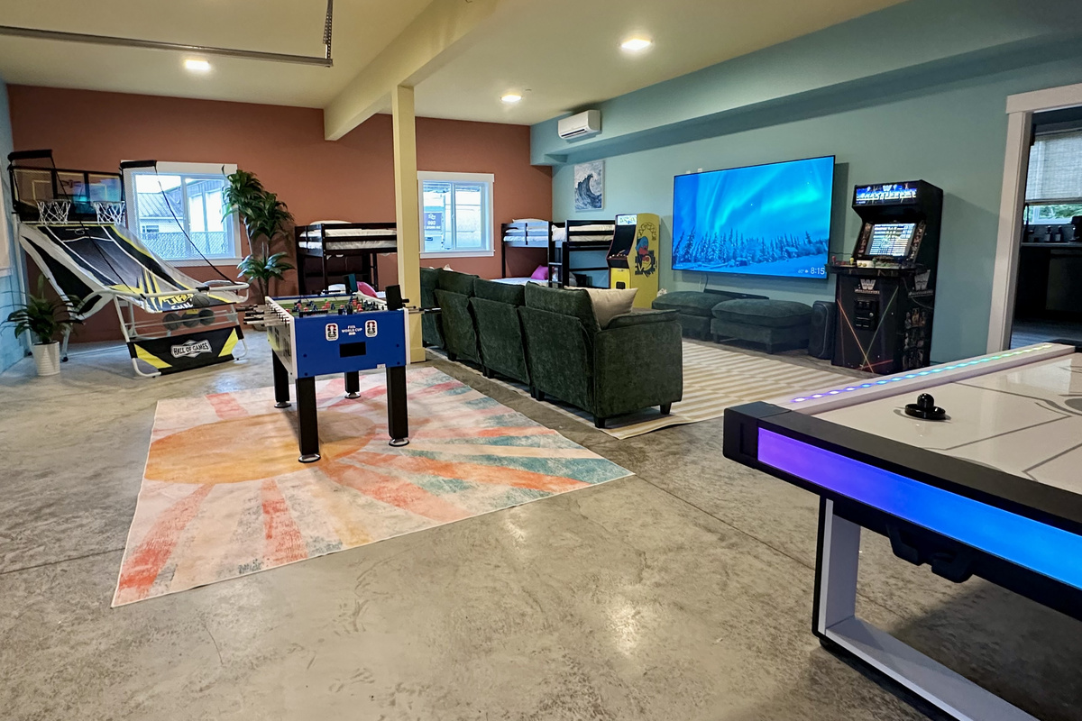The lower level, wide open: game tables, arcade machines and the theater screen all sharing one bright space.