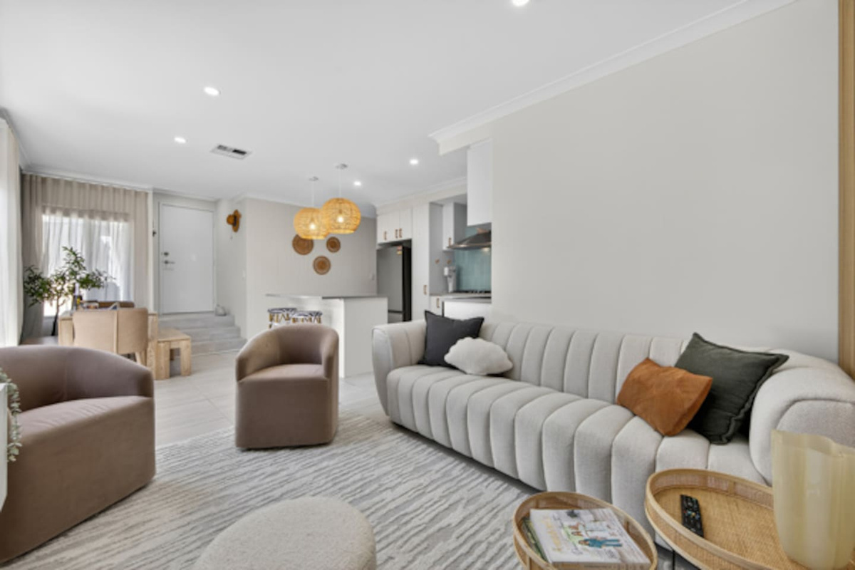 Bright open-plan lounge with a plush sofa and tub chairs, flowing through to the kitchen and dining area.