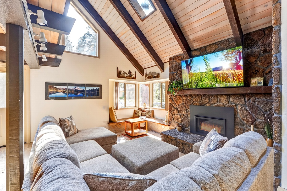The living room is warm and inviting, featuring a cozy fireplace, a large sectional, a comfortable corner nook for additional seating, and a big Smart TV—perfect for relaxing together after a day in Sunriver.
