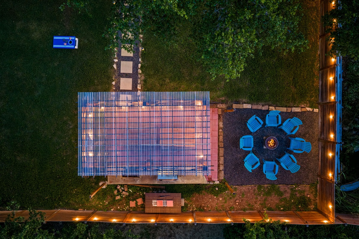 Aerial nighttime view of the backyard featuring a covered BBQ pavilion, glowing fire pit lounge, and spacious fenced yard. Designed for unforgettable evenings, outdoor dining, and relaxing under the Texas stars.