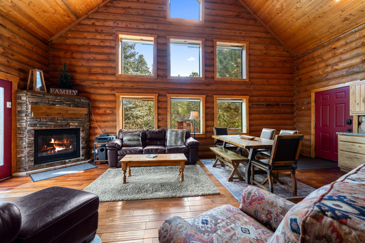 Soaring log cabin living room with vaulted ceilings, large windows, and a gas fireplace.