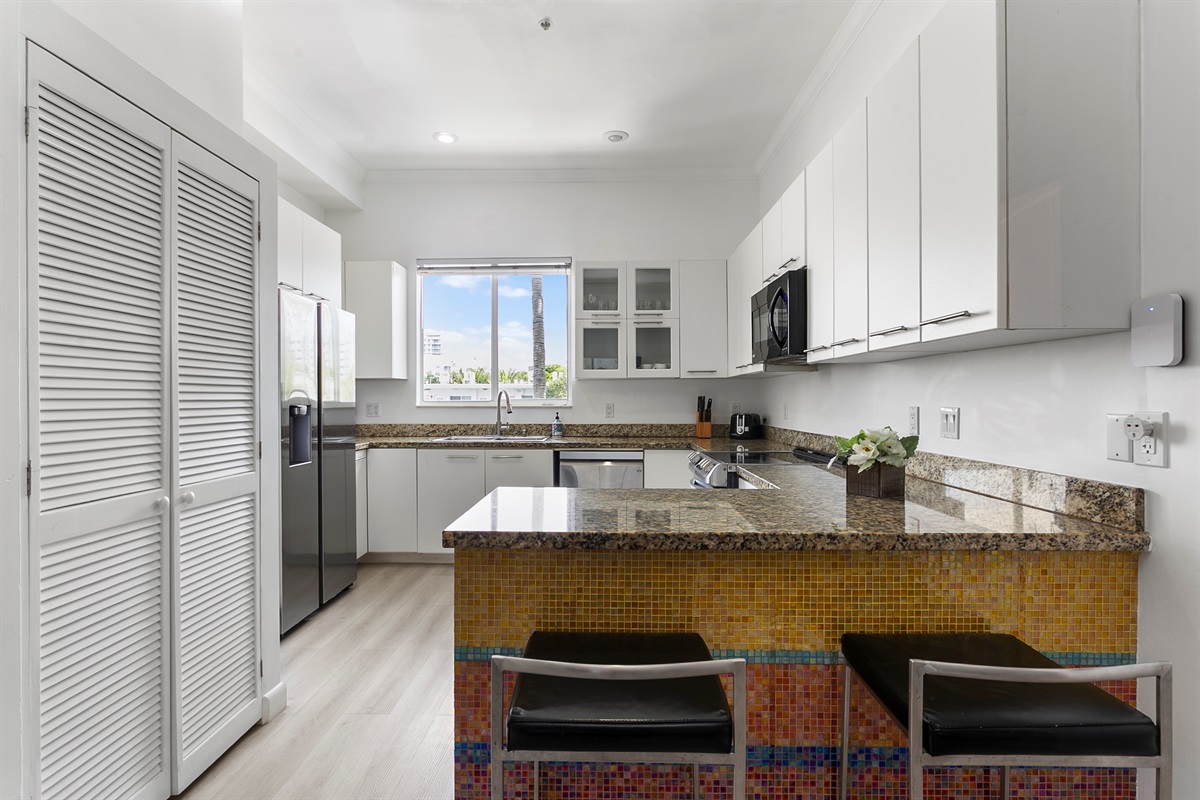 Mosaic tiled kitchen with modern appliances and breakfast counter. LG laundry tower behind closet doors
