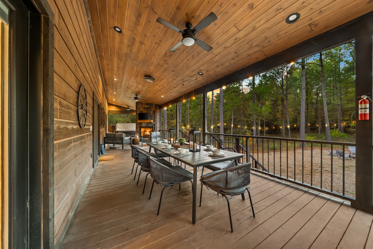 Al fresco dining with a beautifully set table, warm lighting, and peaceful views of the trees and firelight below.