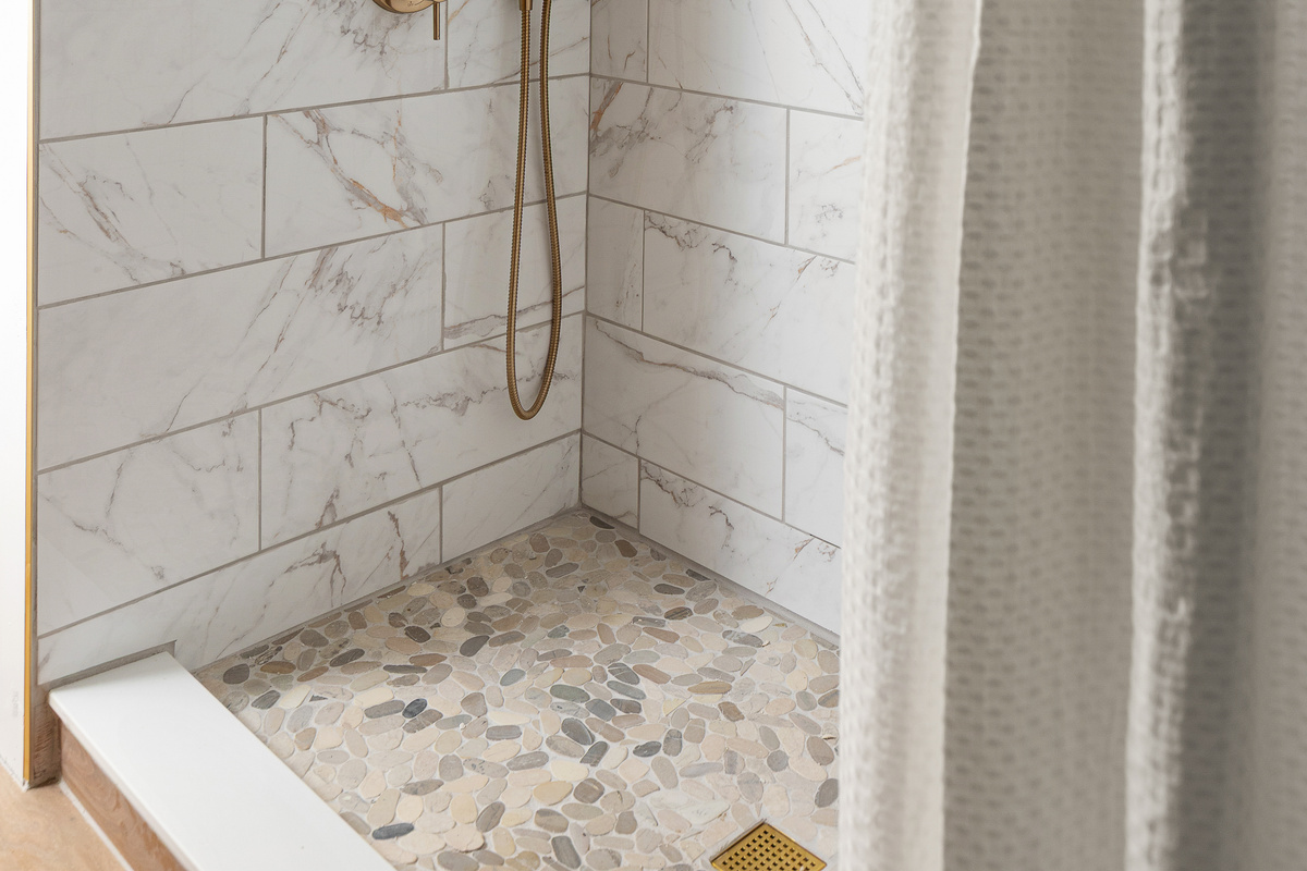 Custom tile walk-in shower featuring a rainfall shower head, handheld wand, pebble stone floor, and warm brass fixtures. A spa like space designed to help you relax after a day at the beach, pool, or local wineries. (The shower now has custom glass doors)