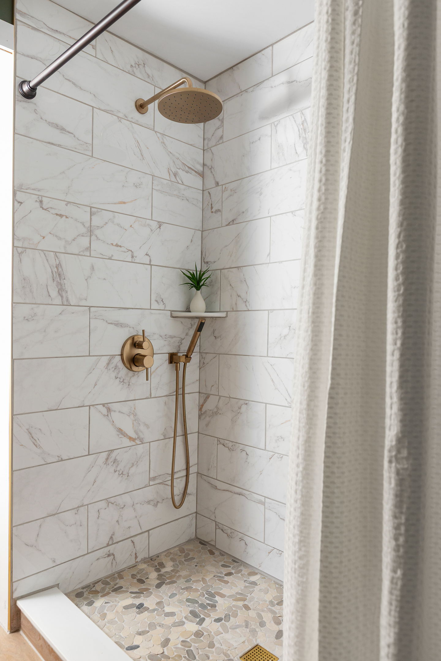 Custom tile walk-in shower featuring a rainfall shower head, handheld wand, pebble stone floor, and warm brass fixtures. A spa like space designed to help you relax after a day at the beach, pool, or local wineries. (The shower now has custom glass doors)