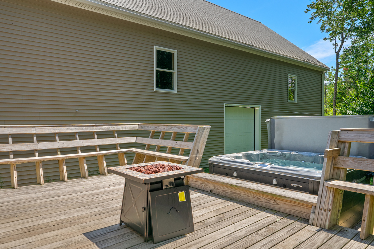 Experience the full layout of the outdoor wooden deck entertainment zone. View details the expansive wrap-around integrated wooden bench seating, the central propane fire table, and the side-by-side placement of the private 6-person hot tub.