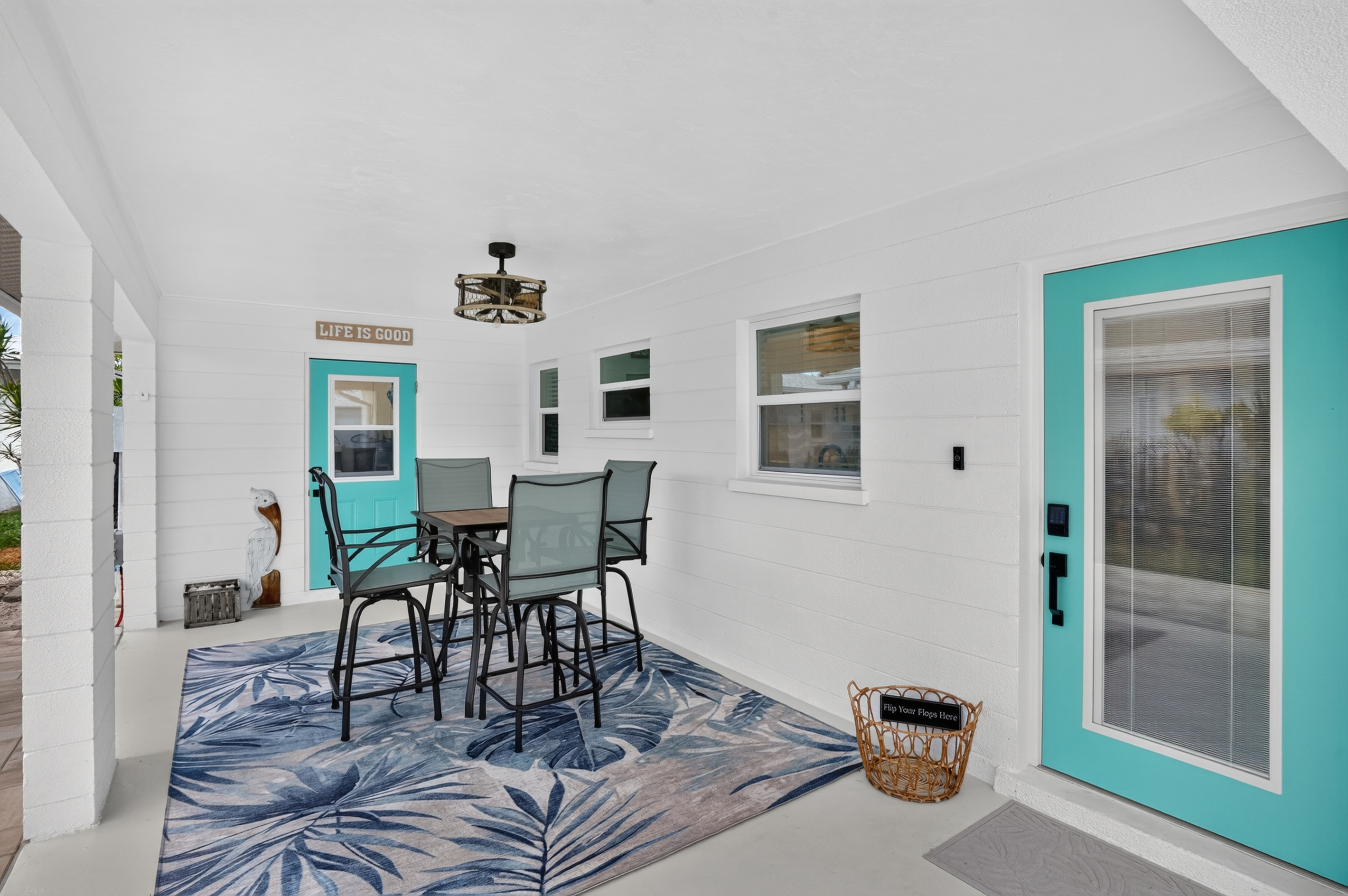 The covered outdoor area includes a cheerful outdoor dining area with a high-top table, palm-leaf rug and signature teal doors.

