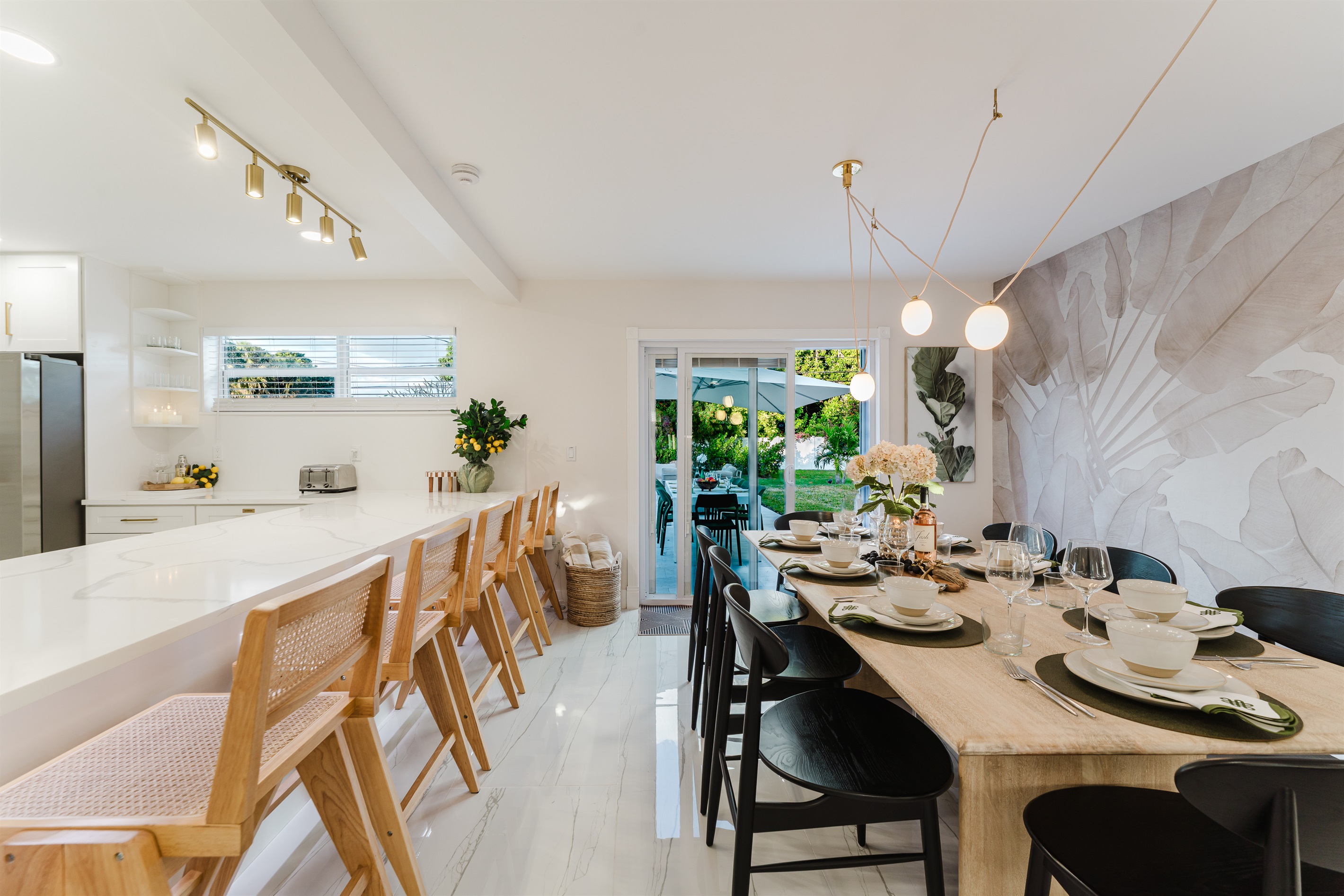 Designer dining room featuring a Gwyneth Paltrow GOOP statement light, custom wallpaper, and seating for 12. Backlit counter seating and seamless access to the patio and backyard make this space ideal for family meals and entertaining.