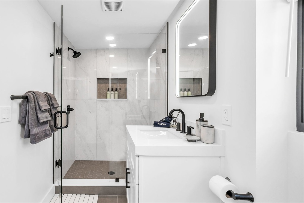 Step into a brand-new, spa-inspired primary bathroom featuring a sleek glass-enclosed walk-in shower with rainfall showerhead, designer vanity with LED mirror, and elegant finishes throughout.