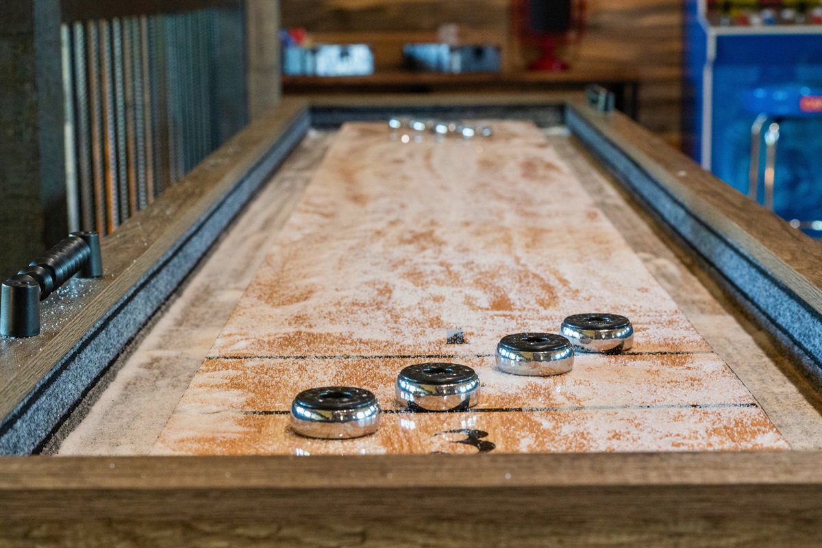 The shuffleboard table, amidst the game room, promises a fun challenge with its well-worn playing surface and pucks ready for action.