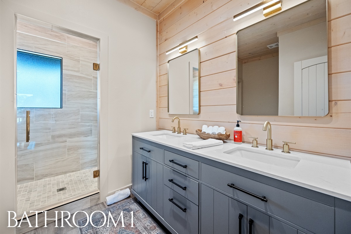 Bathroom 1 with dual sinks, gold fixtures, and walk-in shower.