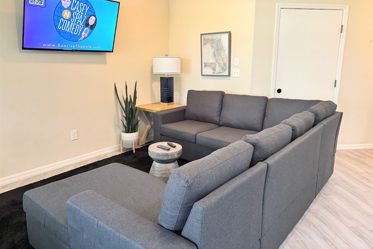 Comfortable living room featuring a large sectional sofa, wall-mounted TV, and clean modern flooring.