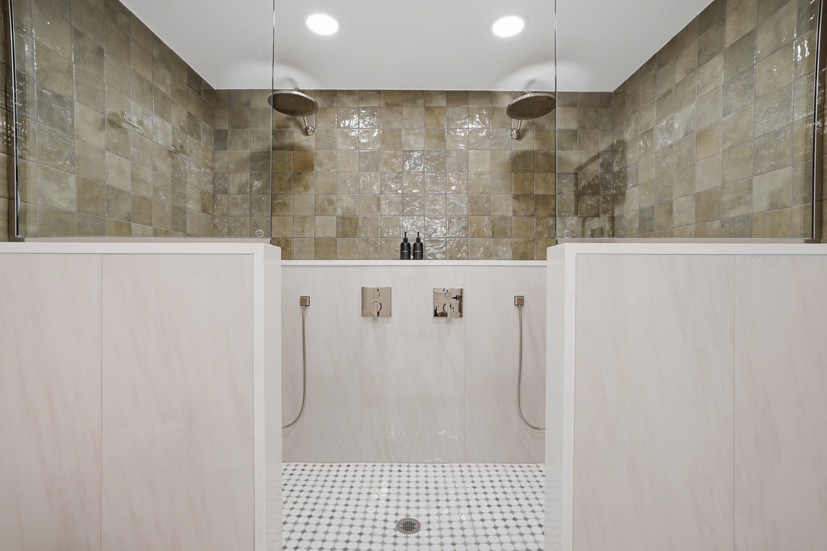 Spa-inspired dual shower area featuring elegant stone tile walls, a sleek glass divider, and a clean, modern layout. Bright, minimalist design with a calm, hotel-like feel for a refreshing and relaxing experience.