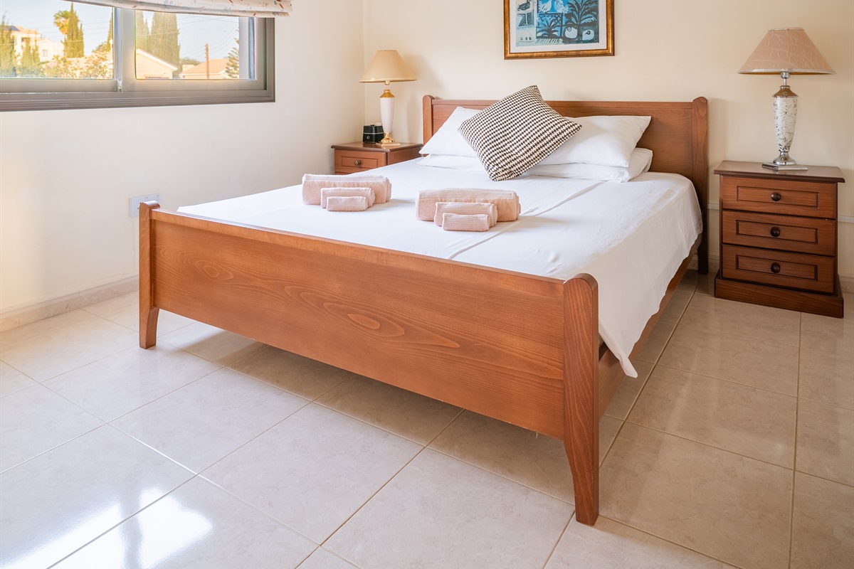 Double bedroom with a window facing the front of the villa. The room has spacious closets, a ceiling fan, a dedicated AC/heating unit, and a Bluetooth-enabled speaker/alarm clock combo.