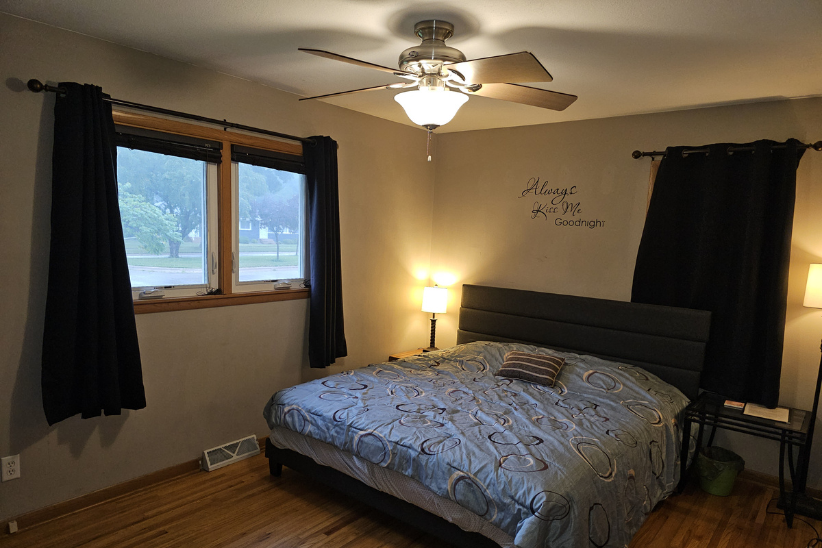 Master bedroom on the main floor with king bed, ceiling fan, alarm clock and a smart tv.