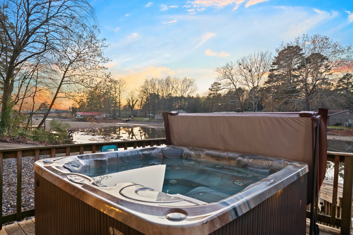 The hot tub offers a peaceful spot to soak while enjoying a beautiful view of the surrounding trees and water.