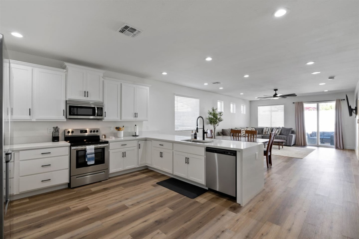 Full kitchen with stainless steel appliances, white cabinetry, dishwasher, plenty of counter space for everyday meals and overview to living area