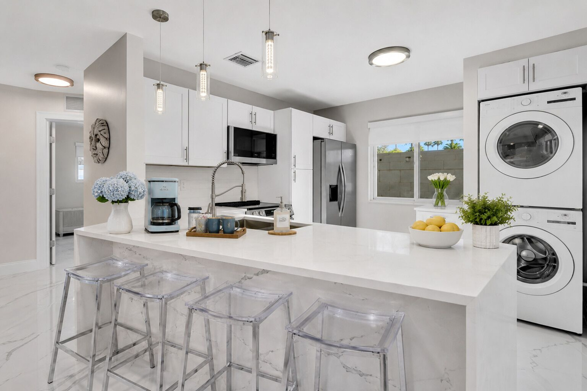 Fully stocked modern kitchen with a large island and seating for four, stainless steel LG appliances, drip coffee maker, and convenient in-unit washer and dryer.