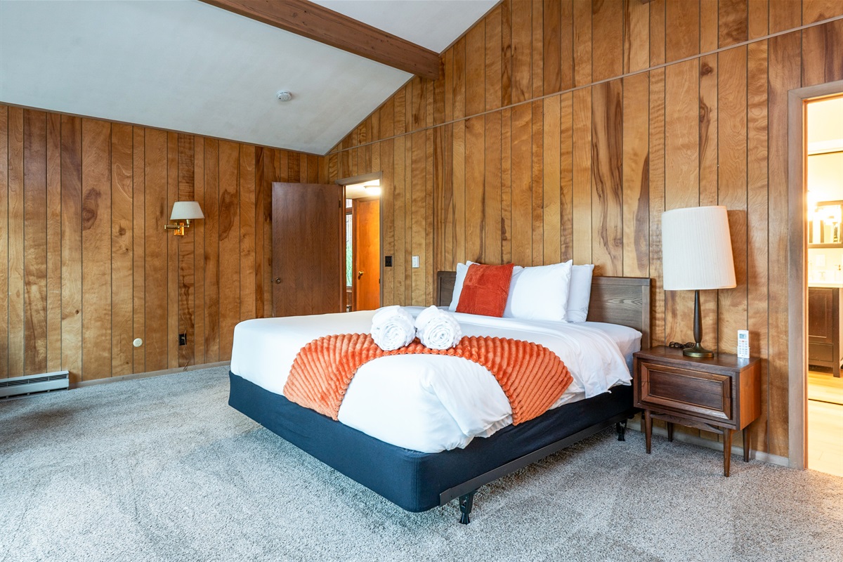 Bright and inviting bedroom with wood-paneled walls, soft carpeting, and bold orange accents that add a pop of color and charm.