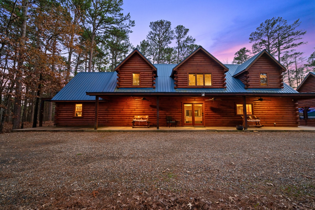 A wide shot shows the cabin, driveway, and open space nestled comfortably within the trees.