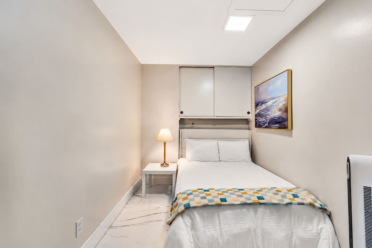 Cozy third bedroom with a full-size bed, built-in storage, bedside table and reading lamp.